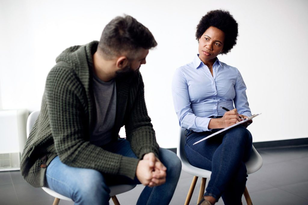 A young woman doing debt counselling work by speaking to a young man while sitting next to him.